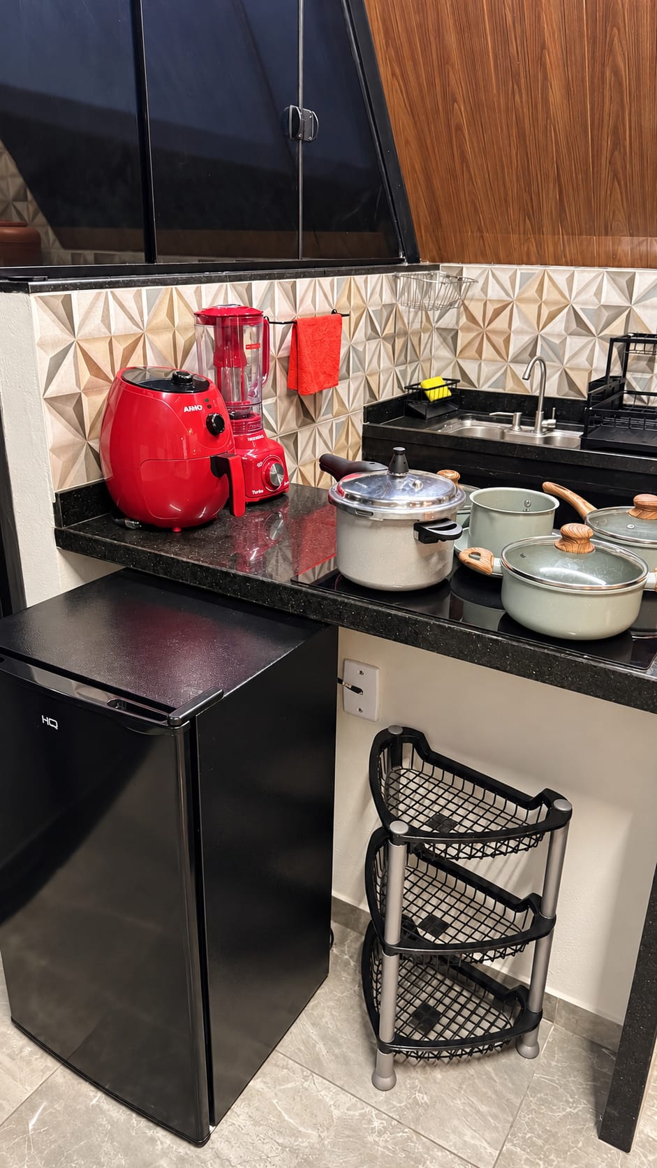 Cozinha com bancada preta, panelas, air fryer e liquidificador, e o frigobar embaixo.