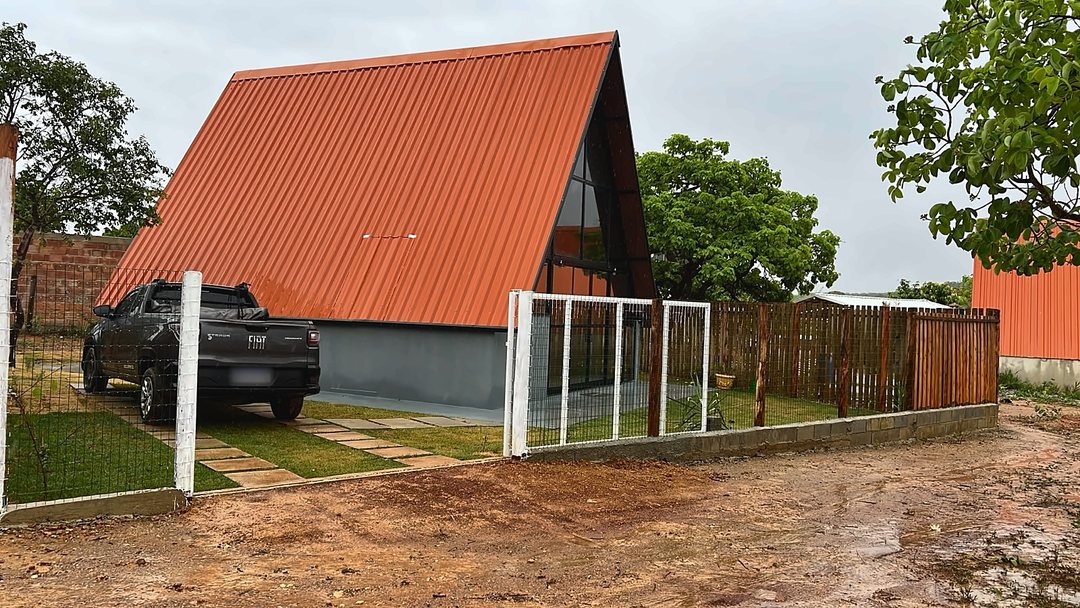 Chalé A-frame de telhado terracota ao lado de árvores do cerrado, em dia nublado.