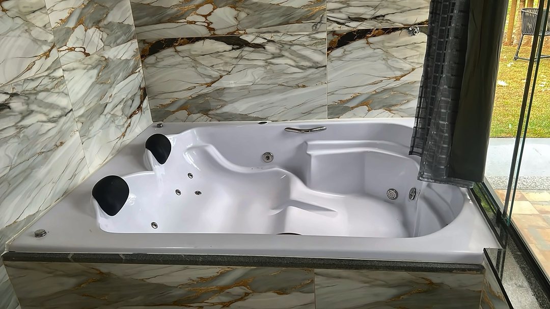 Hidromassagem com revestimento de porcelanato marmorizado, encostada na parede de vidro do chalé.
