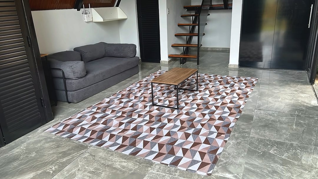 Sala do chalé com sofá-cama cinza, mesa de centro e a escada de madeira que leva ao mezanino.