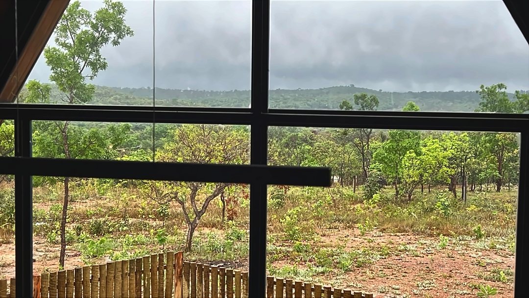 Vista do cerrado e das colinas, vista de dentro do chalé pela parede de vidro, em dia nublado.
