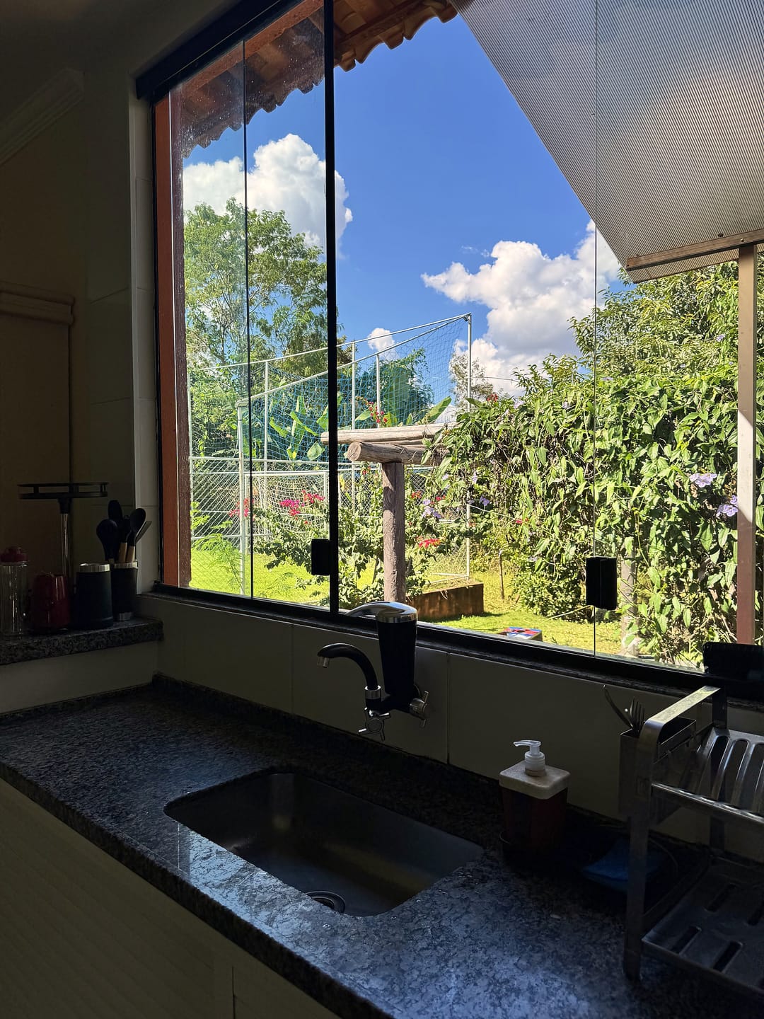 Pia da cozinha sob uma janela grande de vidro, com vista para o jardim.